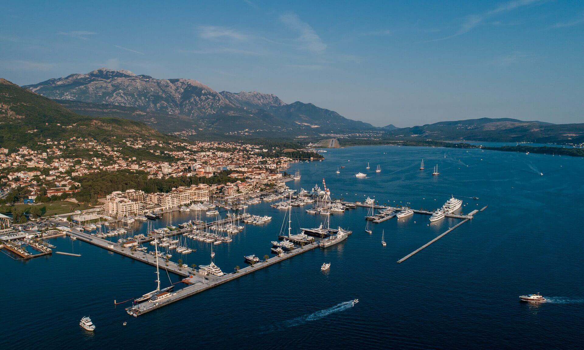 Aerial view of Marina village, Porto Montenegro with boats docked, surrounded by majestic mountains in the background.